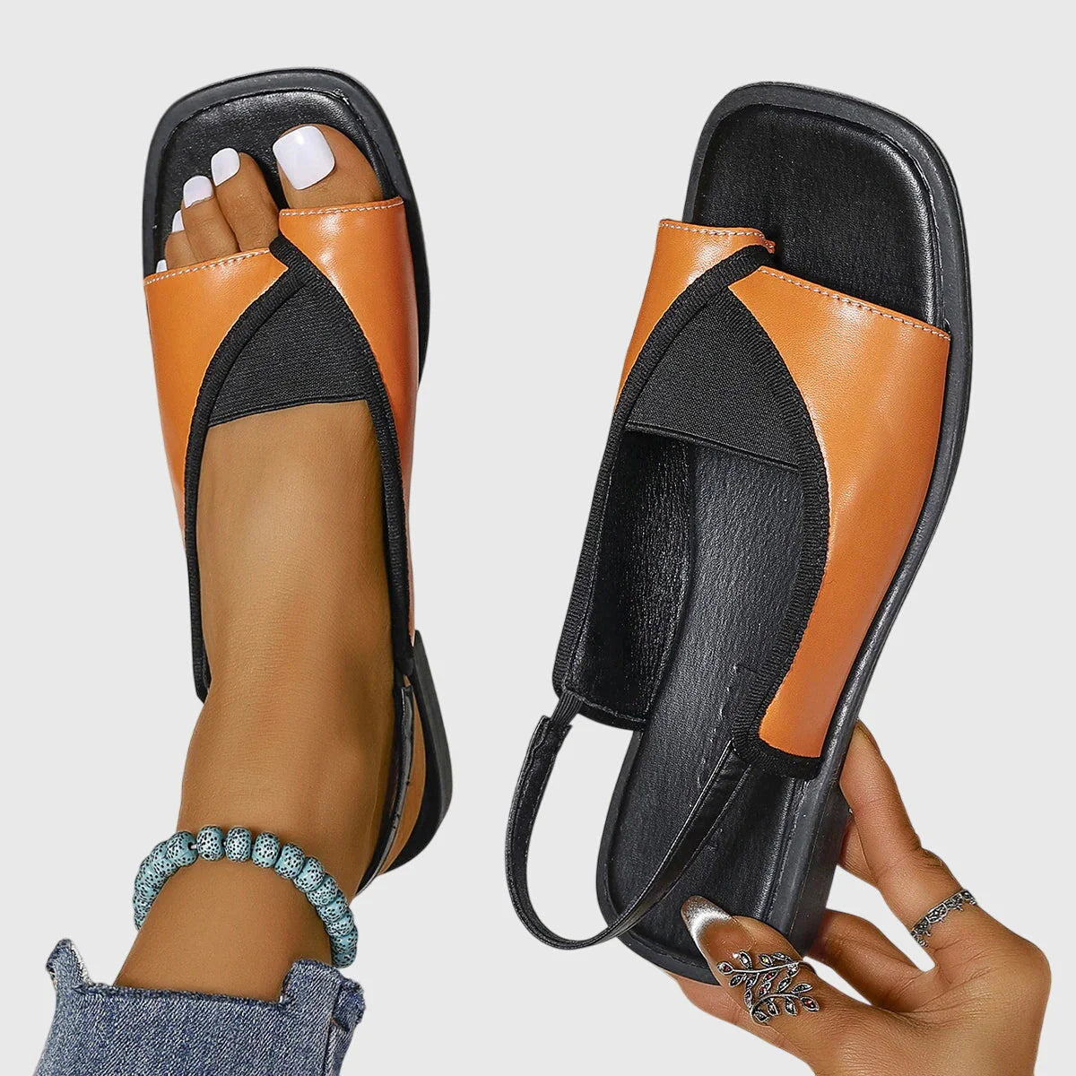 Women's slingback sandals in white and black colourway with toe-loop design and flat sole on wooden deck
