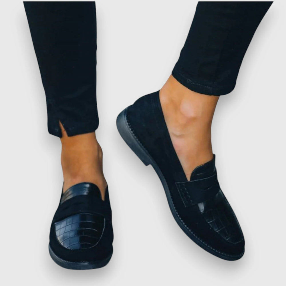 Close-up view of black orthopedic loafers featuring smooth upper and textured croc detailing on vamp