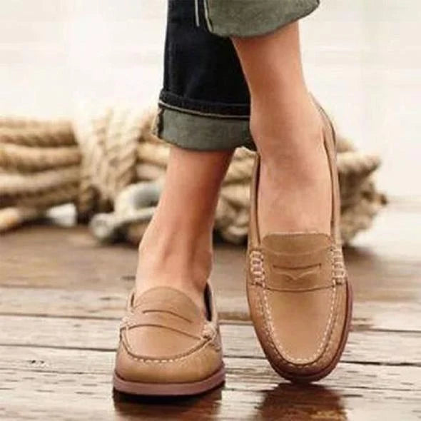 Close-up of women's slip-on loafers displaying smooth finish, penny strap detail, and low-profile flat sole