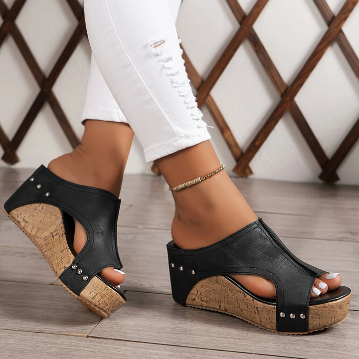 Elegant wedge sandals with cork platform heel and black upper with studded detail worn with white jeans