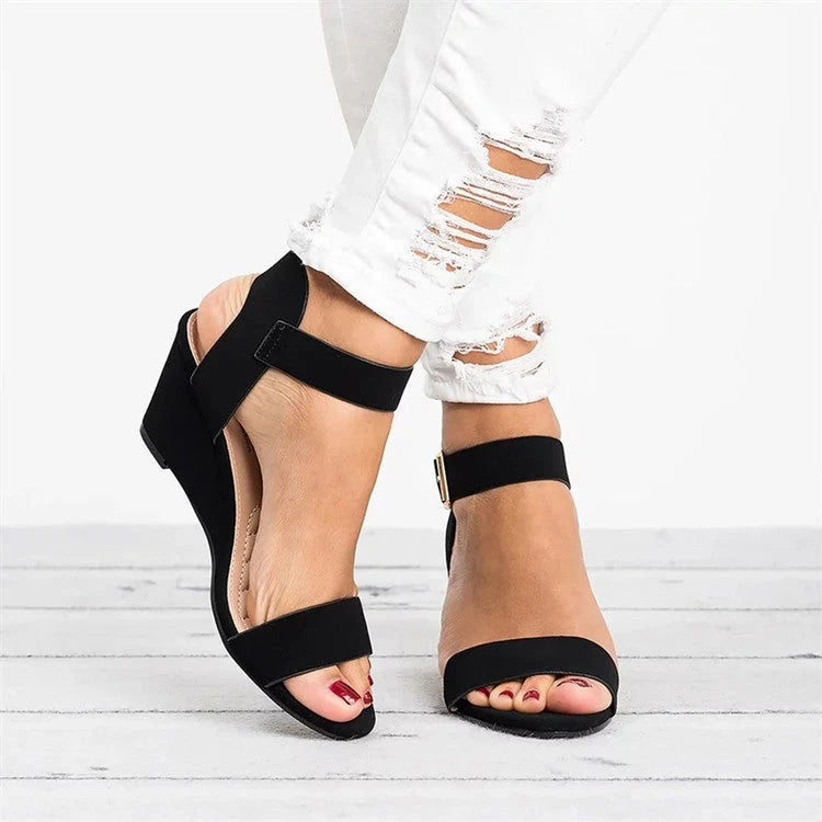 Women's wedge sandals in black with adjustable ankle strap and open-toe design, worn with distressed white jeans