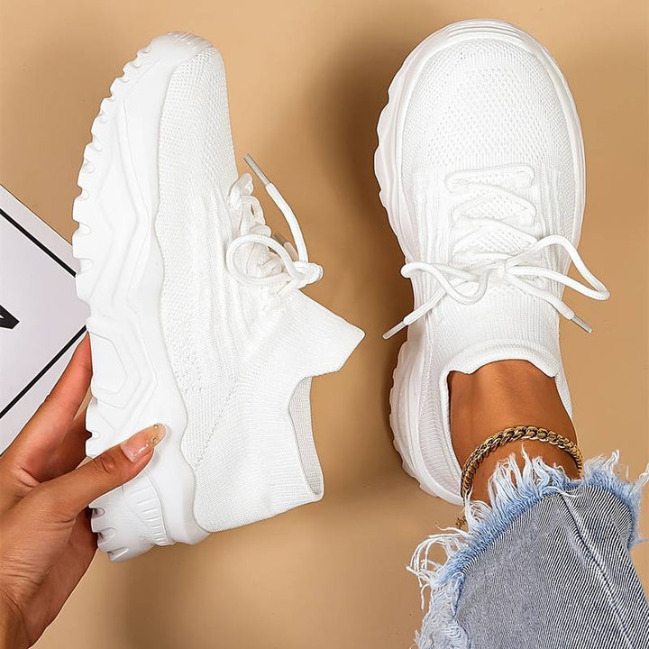 Overhead view of white women's orthopedic shoes for women with chunky rubber sole and breathable mesh upper on beige background