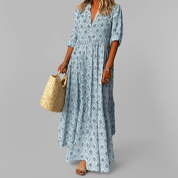 Woman wearing paisley print maxi dress with V-neckline and three-quarter sleeves holding woven bag