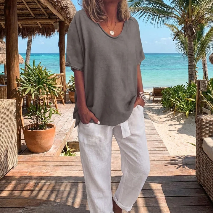 Woman wearing a relaxed grey v-neck tee with white linen trousers on a tropical beach boardwalk