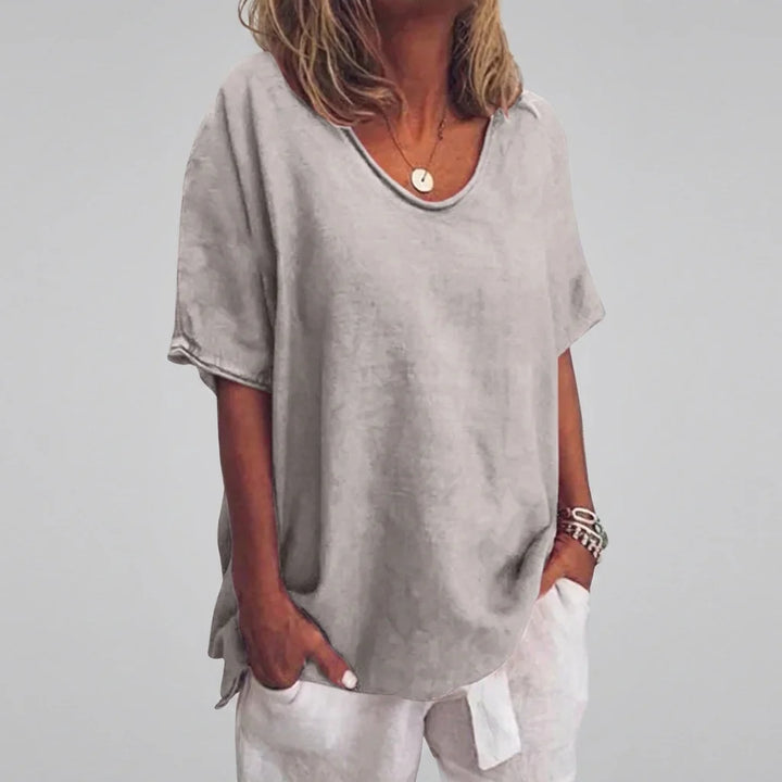 Side angle of women's casual v-neck tee paired with white trousers in beachside setting