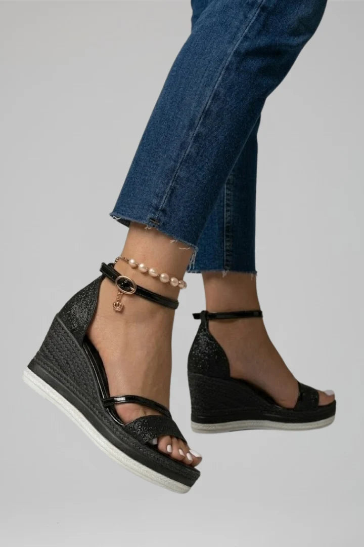 Pair of black platform wedge sandals with ankle straps on neutral background
