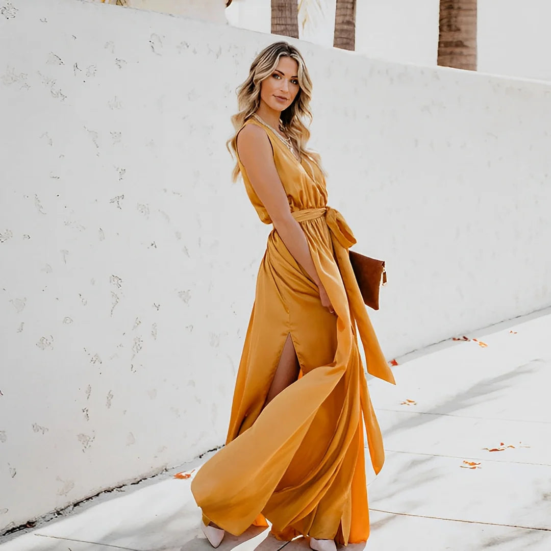 Woman wearing golden yellow sleeveless maxi dress with tie waist and side slit outdoors